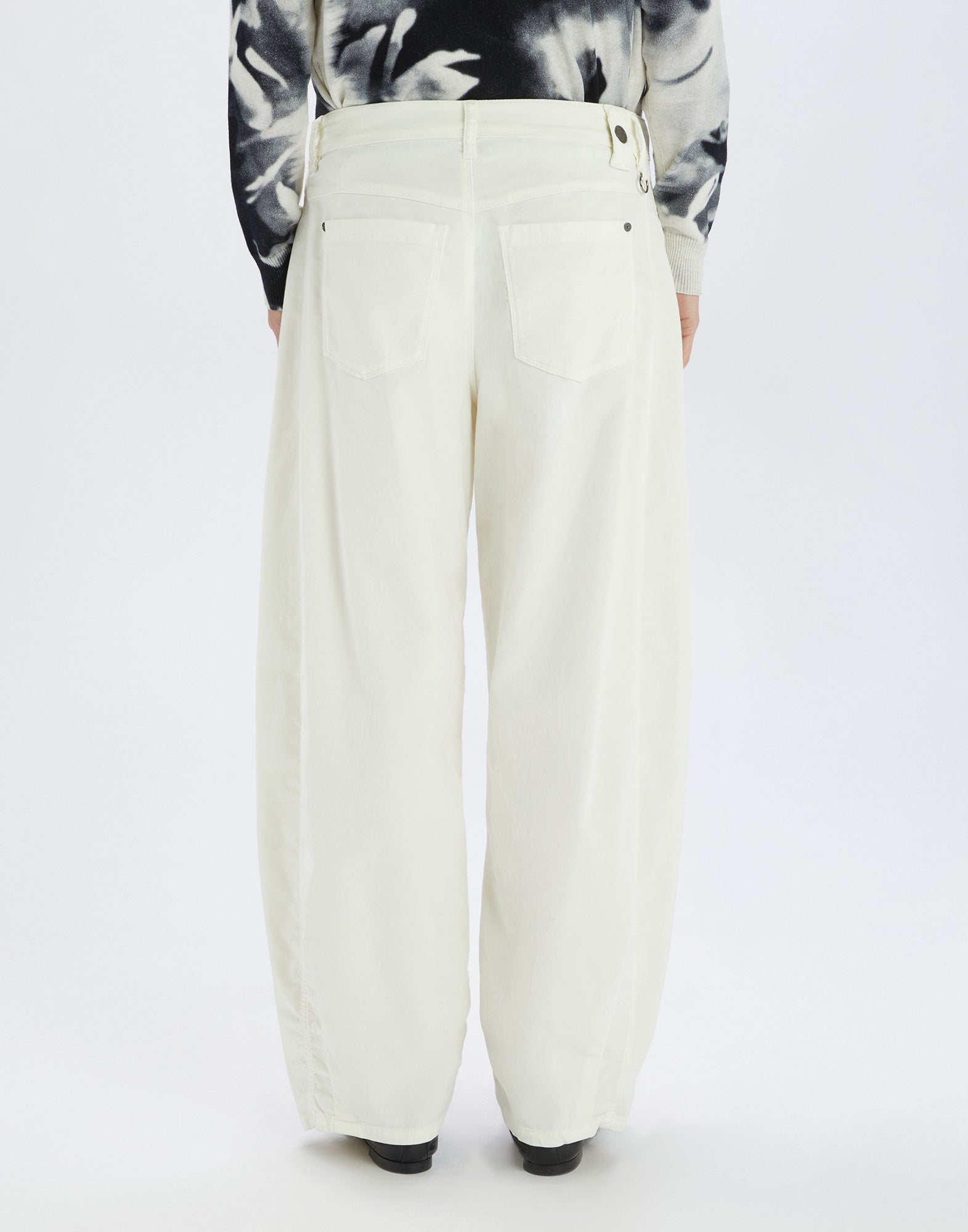 Back view of the GOTLAND trousers: wide, ankle-length trousers in cream white with back patch pockets, visible seams, and waistband with belt loops, worn by a person.