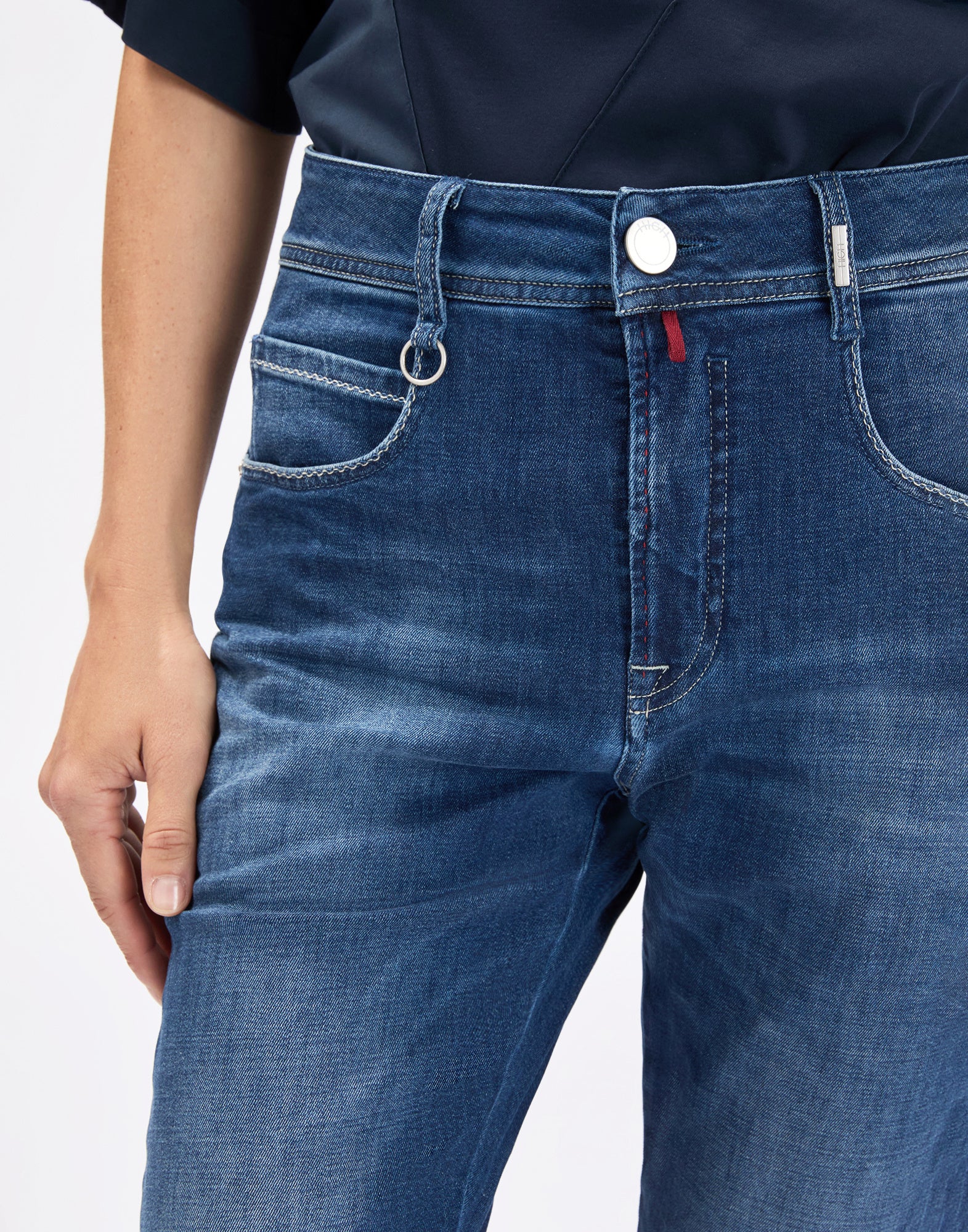 Detailansicht: Person trägt die Jeans OUR-GIRLS frontal, zeigt mittelhohen Bund mit Gürtelschlaufen, Knopf, asymmetrischem Frontverschluss, Vordertaschen mit Münztasche und heller Vintage-Waschung.