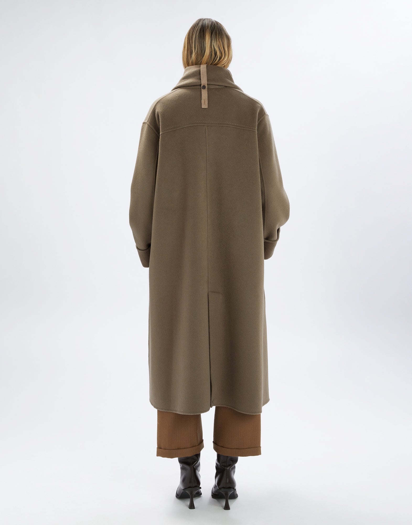 Back view of the SPIRE coat with oversized fit, visible topstitching, and high collar with removable tab, worn by a person.