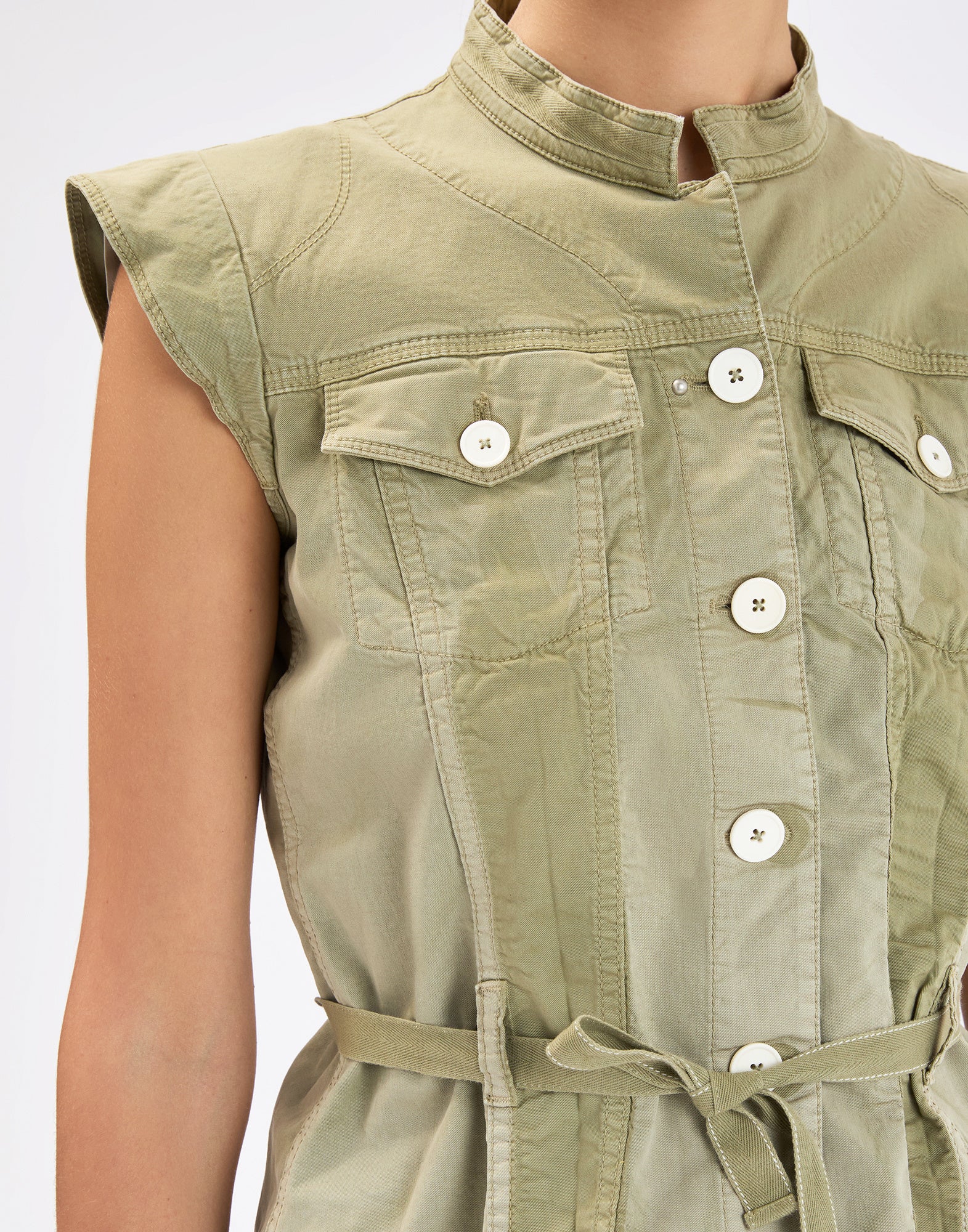 Detail frontal view: model wearing sleeveless, fitted RAISE UP denim jacket in olive green gradient with stand collar, visible stitching, button placket, chest flap pockets, and fabric belt.