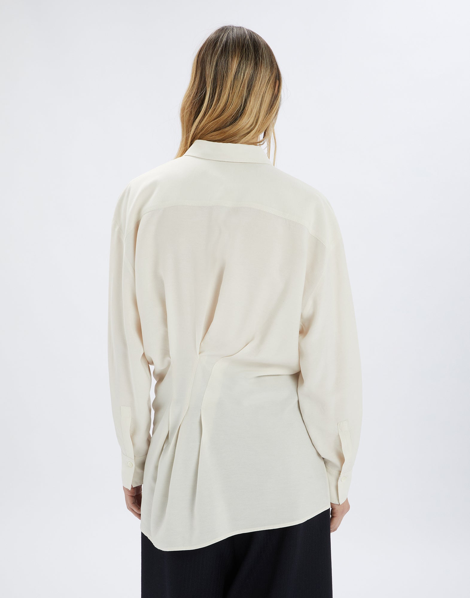Back view of a person wearing the SKYLARK blouse; cream-colored, loose-fitting shirt with back pleats, long sleeves, and tall collar.
