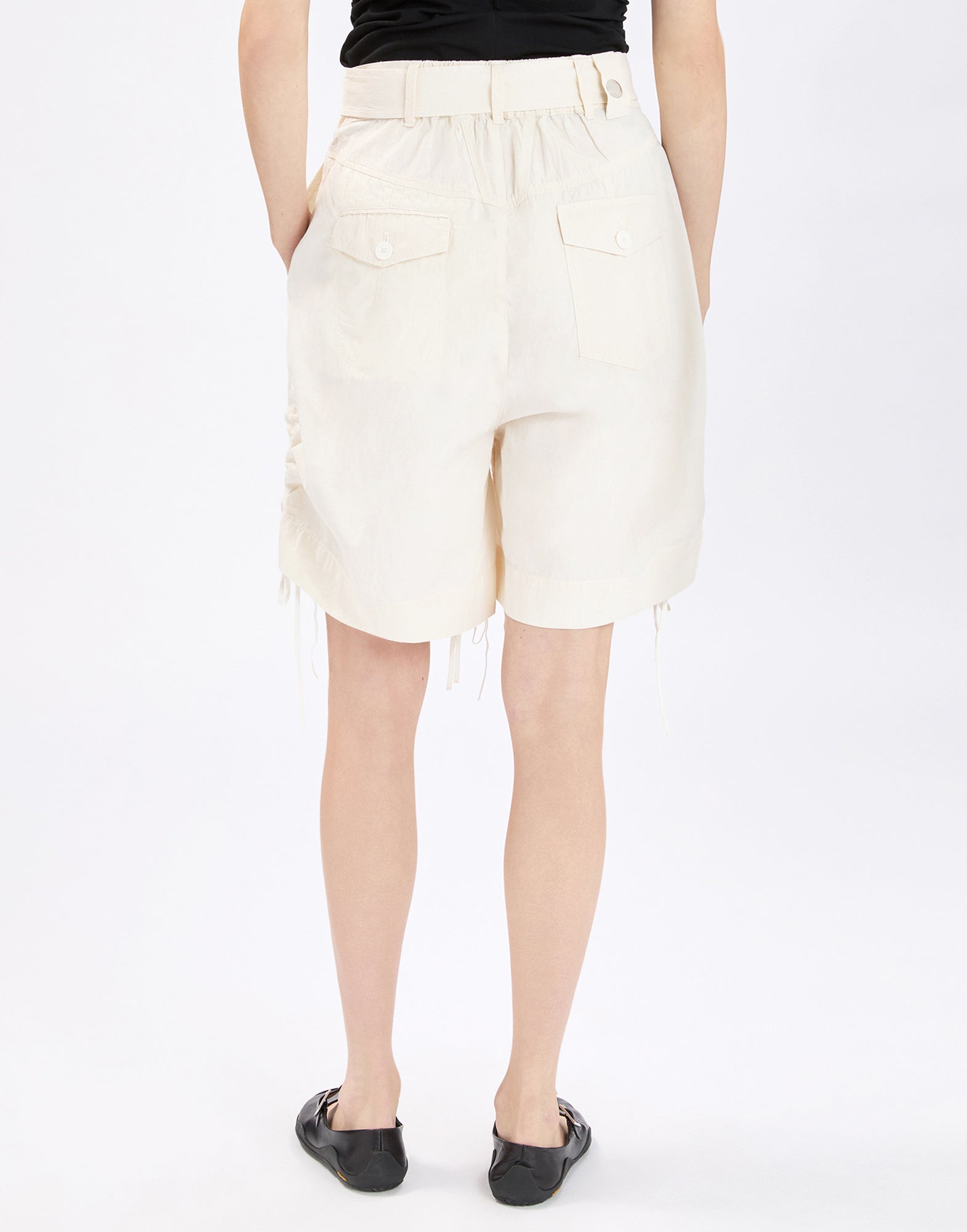 Rear view: Person wearing cream ORDER Bermuda shorts in cotton poplin with high waist, wide belt loops, two back flap pockets with buttons, and side drawstrings at the hem.