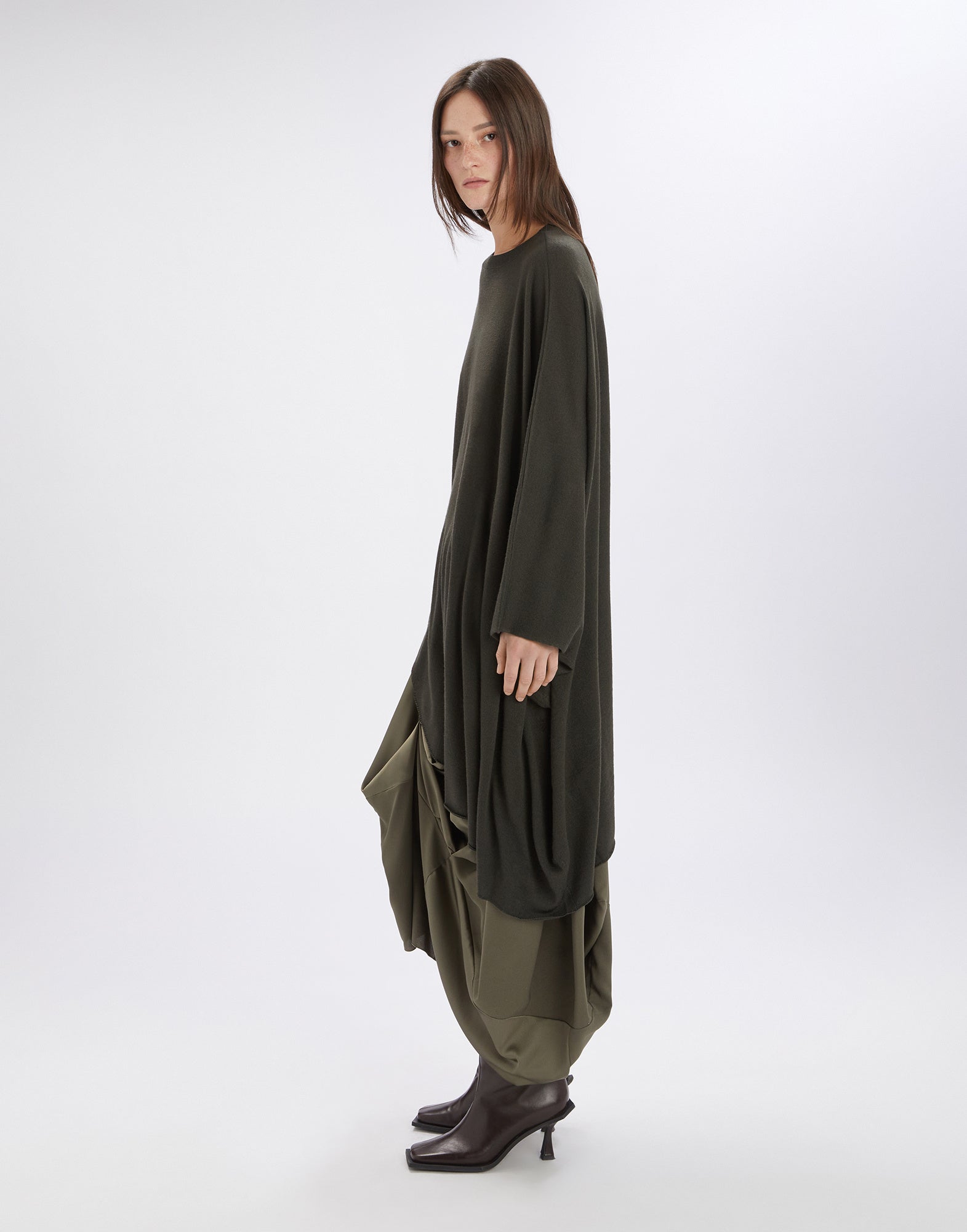 Seitenansicht: Person trägt ON SET Tunika aus Wollmischung in dunklem Olivgrün mit asymmetrischem, fließendem Schnitt, langem Arm und weitem, elegantem Saum.